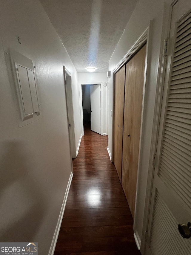 corridor featuring dark wood finished floors, a textured ceiling, electric panel, and baseboards