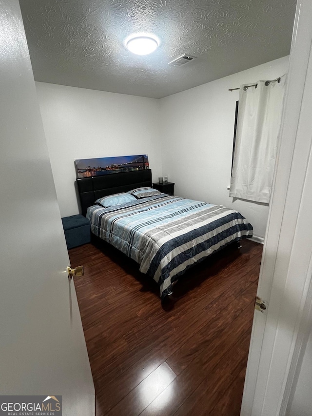 bedroom featuring wood finished floors, visible vents, and a textured ceiling