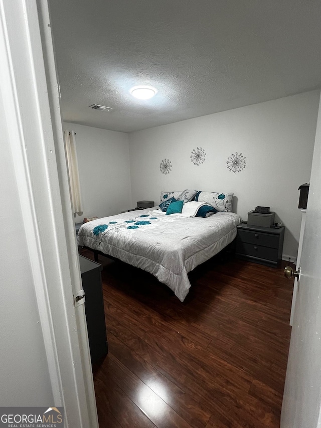 bedroom featuring visible vents, a textured ceiling, and dark wood-style floors