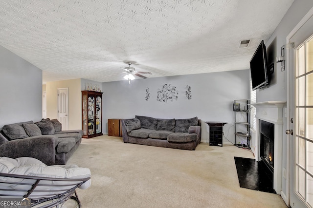 carpeted living area with a fireplace with flush hearth, a ceiling fan, visible vents, and a textured ceiling