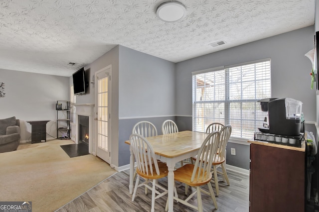 dining area featuring visible vents, a fireplace with flush hearth, baseboards, and light wood-style flooring