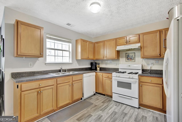 kitchen with white appliances, visible vents, a sink, under cabinet range hood, and dark countertops