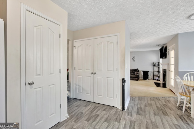 corridor with light wood-style floors and a textured ceiling