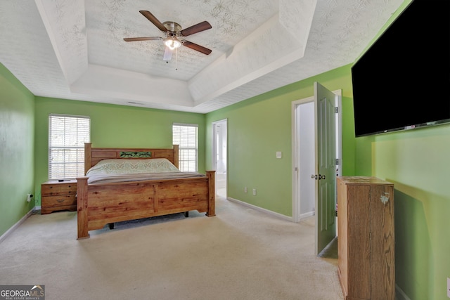 bedroom with multiple windows, a textured ceiling, light colored carpet, and a tray ceiling