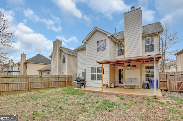 back of house featuring a yard, a chimney, a fenced backyard, and a ceiling fan