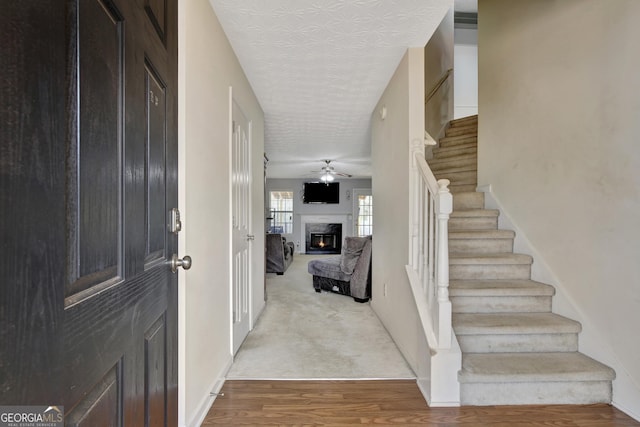 entryway featuring a high end fireplace, stairs, wood finished floors, a textured ceiling, and a ceiling fan