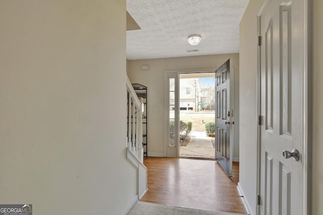 entryway featuring stairway, a textured ceiling, baseboards, and wood finished floors