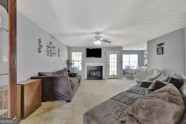 living area with light carpet, a fireplace, a textured ceiling, and ceiling fan