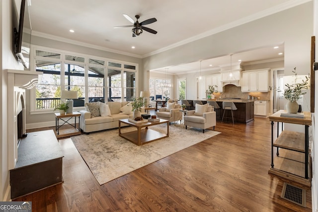 living room with visible vents, dark wood-type flooring, ornamental molding, and a ceiling fan