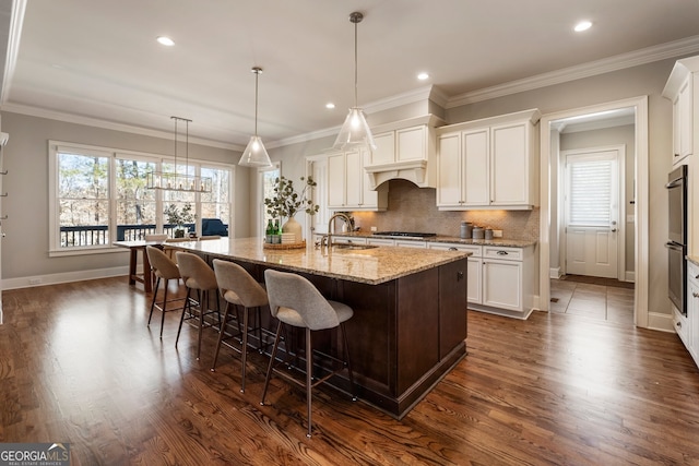 kitchen featuring dark wood finished floors, a center island with sink, backsplash, and a sink