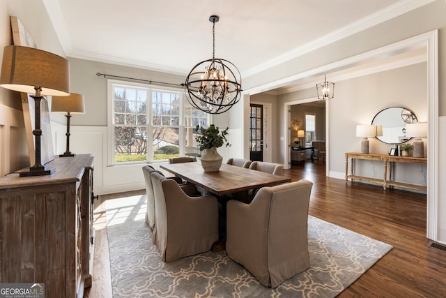 dining space featuring a wainscoted wall, dark wood-type flooring, an inviting chandelier, and ornamental molding