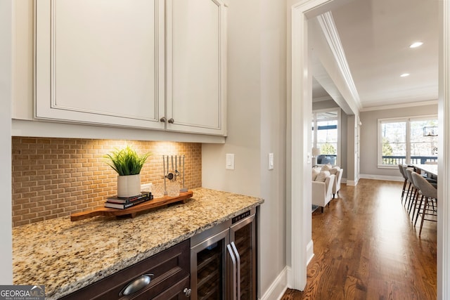 kitchen with beverage cooler, light stone countertops, dark wood finished floors, crown molding, and tasteful backsplash