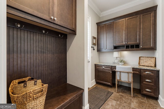 mudroom with stone finish flooring, baseboards, built in desk, and ornamental molding