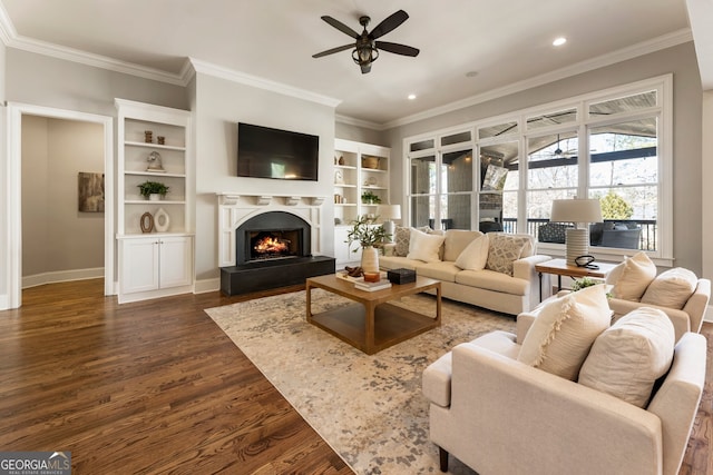 living room featuring a warm lit fireplace, dark wood-type flooring, a ceiling fan, and crown molding