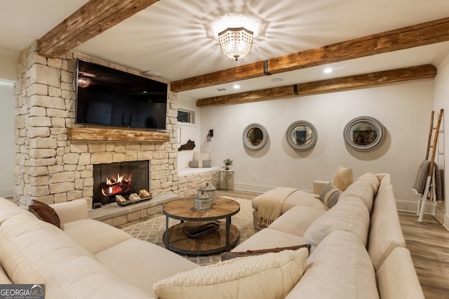 living area featuring a stone fireplace, beamed ceiling, wood finished floors, and baseboards