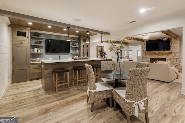 dining space featuring beamed ceiling, visible vents, light wood-style flooring, a fireplace, and wet bar