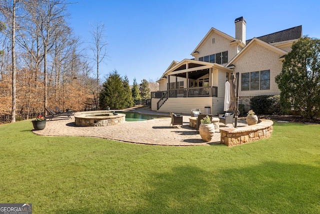 back of property featuring a patio, a lawn, a chimney, and an outdoor fire pit