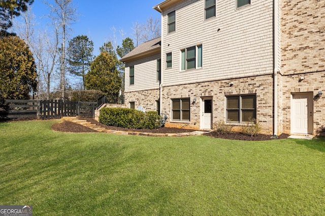 back of house featuring a yard, fence, and brick siding