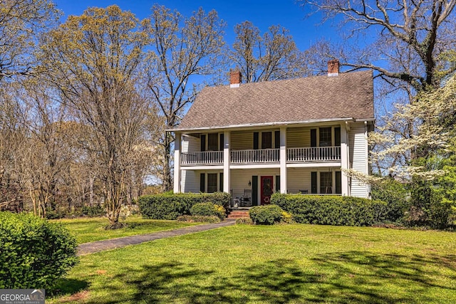 view of front of property with a chimney, a porch, a front yard, and a balcony