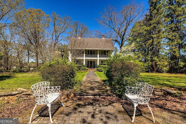 back of property with a balcony, a chimney, and a lawn