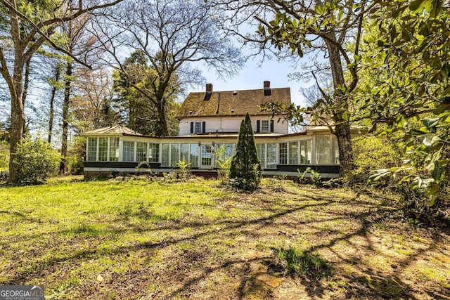 back of house with a lawn, a sunroom, and a chimney