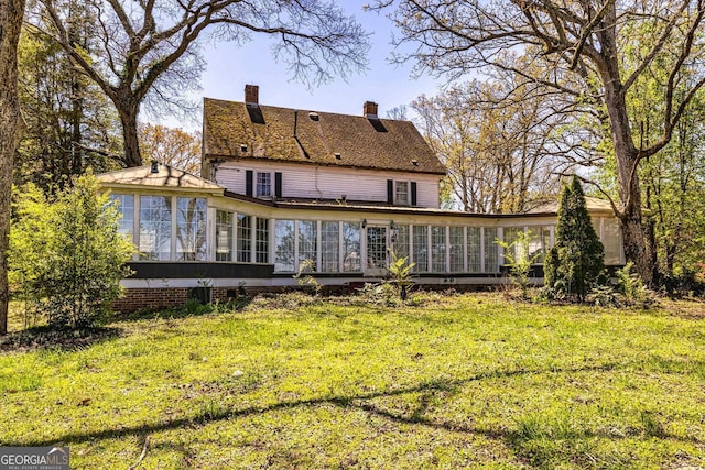 back of property featuring a yard, a chimney, and a sunroom