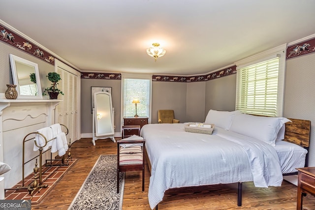 bedroom featuring baseboards, a fireplace with flush hearth, wood finished floors, and crown molding