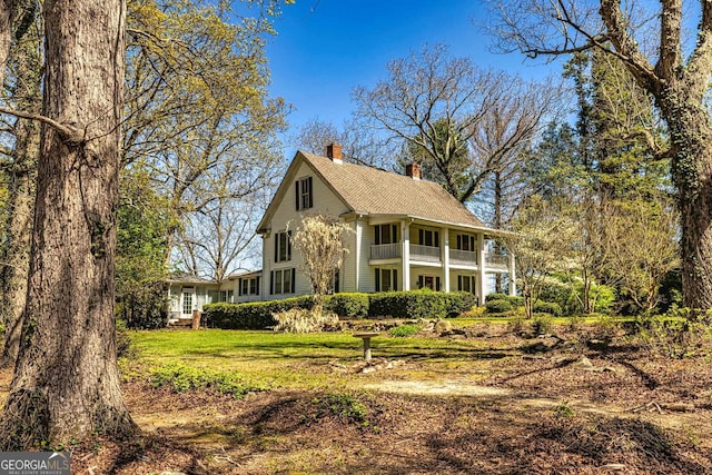 view of front of property featuring a chimney, a balcony, and a front yard