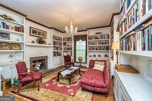 living area featuring built in features, wood finished floors, crown molding, a brick fireplace, and a notable chandelier