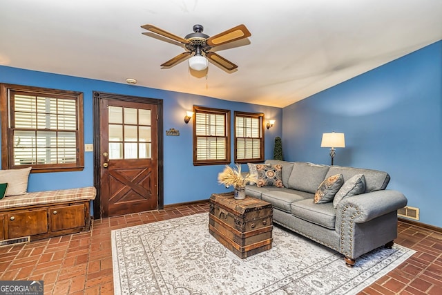 living area featuring brick floor, baseboards, visible vents, and ceiling fan