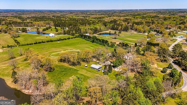 drone / aerial view with view of golf course, a view of trees, and a water view