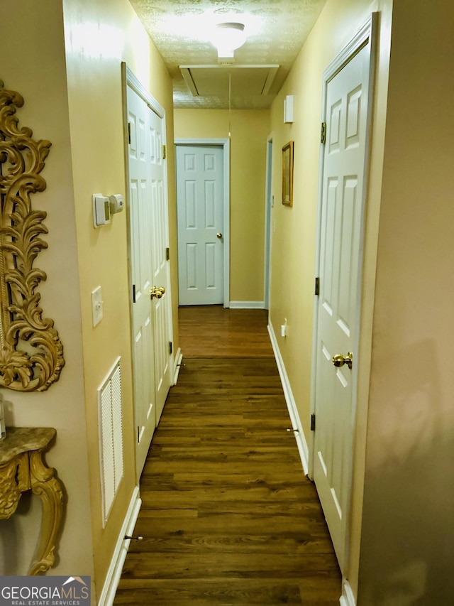 hall featuring visible vents, baseboards, dark wood-type flooring, and attic access