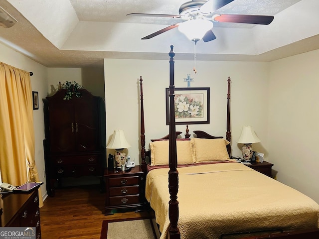 bedroom with a tray ceiling, a ceiling fan, dark wood-style flooring, and a textured ceiling