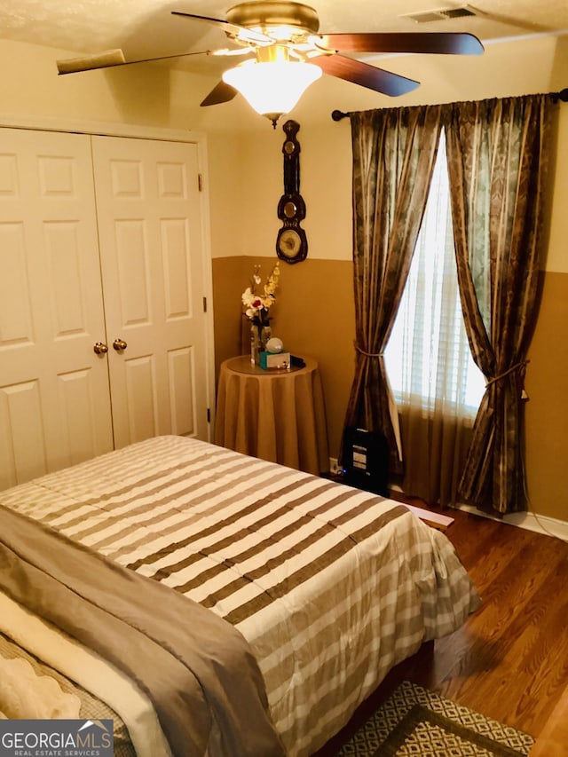 bedroom with a ceiling fan, visible vents, dark wood-style floors, and a closet