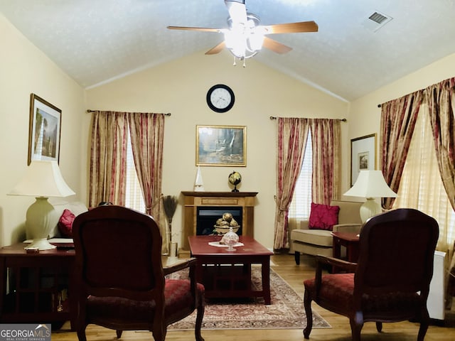 living area with visible vents, a ceiling fan, wood finished floors, a fireplace, and lofted ceiling