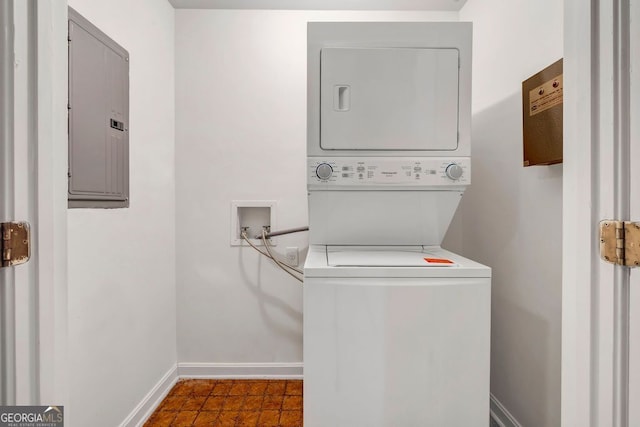 laundry area featuring stacked washer / dryer, electric panel, and baseboards