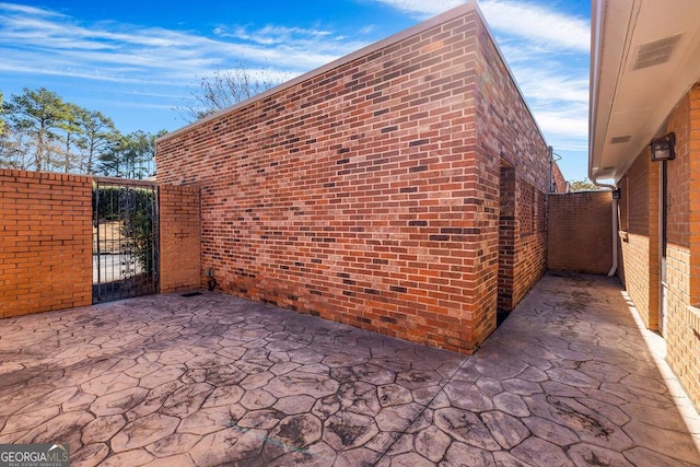 view of side of property featuring a patio, brick siding, and a gate