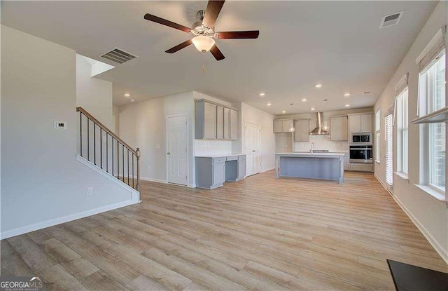 kitchen with visible vents, stainless steel appliances, light wood-type flooring, and wall chimney range hood