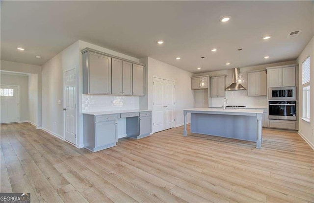 kitchen with visible vents, wall chimney range hood, gray cabinets, appliances with stainless steel finishes, and light wood-style floors