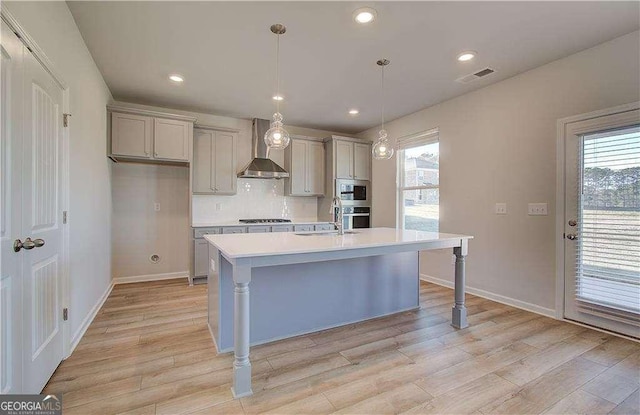 kitchen featuring a center island with sink, plenty of natural light, wall chimney exhaust hood, and light countertops