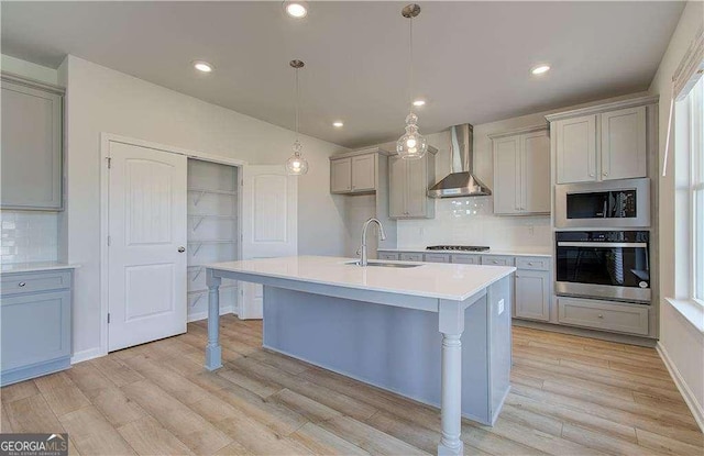 kitchen featuring a sink, gray cabinetry, stainless steel appliances, light wood-style floors, and wall chimney range hood