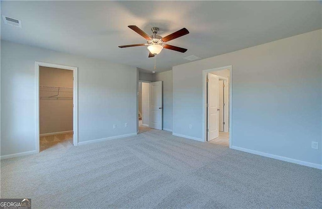 unfurnished bedroom with visible vents, a walk in closet, baseboards, light colored carpet, and a closet