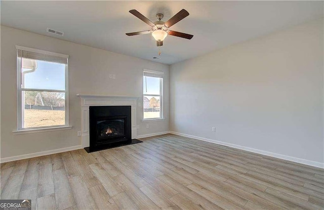 unfurnished living room with visible vents, baseboards, light wood-type flooring, and a fireplace with flush hearth