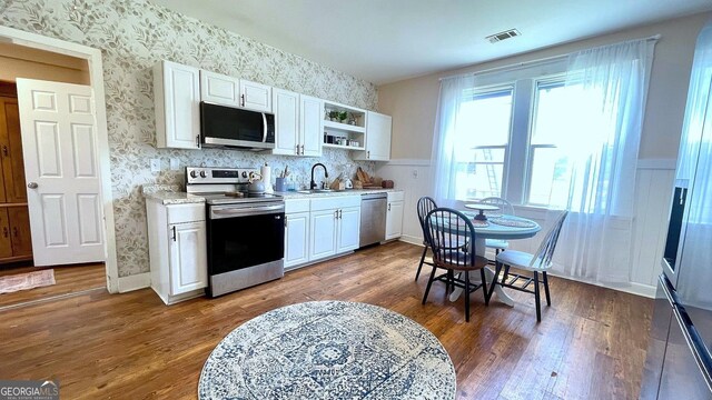 kitchen with stainless steel appliances, open shelves, wallpapered walls, a sink, and light countertops