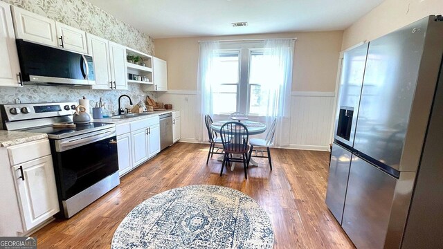 kitchen featuring appliances with stainless steel finishes, open shelves, wainscoting, dark wood finished floors, and a sink