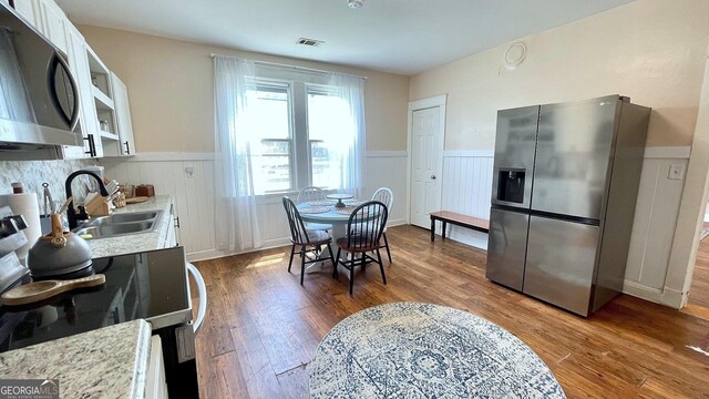 kitchen with stainless steel appliances, wainscoting, a sink, dark wood-style flooring, and light countertops