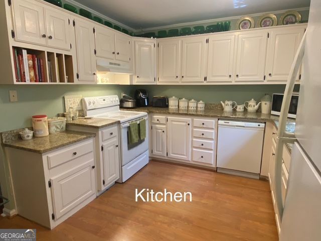 kitchen with white appliances, white cabinets, light wood-style flooring, and under cabinet range hood