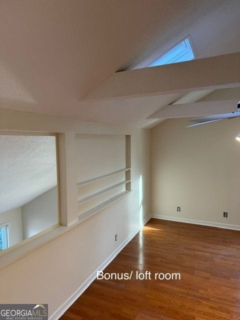 empty room featuring a textured ceiling, lofted ceiling with beams, baseboards, and wood finished floors