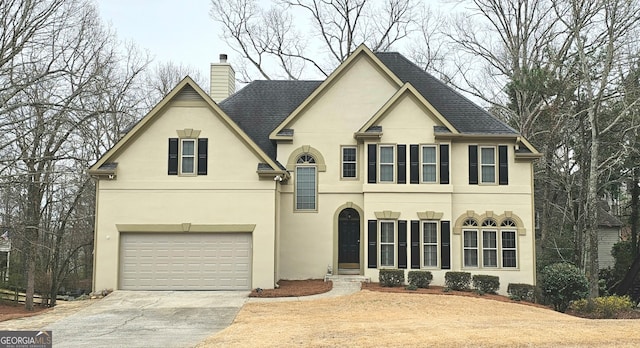 view of front of property featuring roof with shingles, an attached garage, stucco siding, a chimney, and concrete driveway