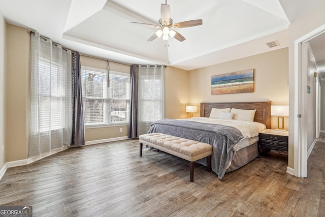 bedroom with a tray ceiling, wood finished floors, visible vents, and baseboards